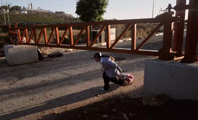 A Palestinian girl walks under an Israeli army gate as she makes her way to school on the first day of the school year, at the entrance to the occupied West Bank village of Qusra, Sunday, Sept. 6, 2026. (AP Photo/Majdi Mohammed)