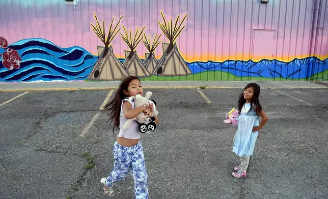 Jaelynn Duran, left, and Abigail Whiteman play in front of a mural at a gas station on the Wind River Reservation near Riverton, Wyo., on Saturday, Aug. 15, 2026. (AP Photo/Thomas Peipert)