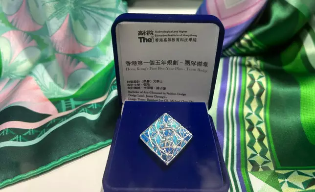The badge design is in the same vein as the tie's theme, featuring a diamond design with metallic lines outlining a star inside, using the blue color of the cover page of "Hong Kong's First Five-Year Plan", with a gradient design creating a three-dimensional effect. Photo by Bastille Post