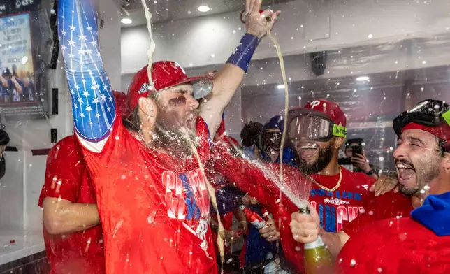 Philadelphia Phillies first baseman Bryce Harper, left, is doused by Garret Stubbs, right, during a celebration in the clubhouse after the team clinched a Wild Card slot in the postseason by defeating the Tampa Bay Rays in a baseball game Sunday, Sept. 27, 2026, in Philadelphia. (AP Photo/Laurence Kesterson)