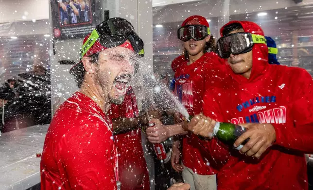 Philadelphia Phillies catcher Garrett Stubbs, left, is doused by teammates during a celebration in the clubhouse after the team clinched a Wild Card slot in the postseason by defeating the Tampa Bay Rays in a baseball game Sunday, Sept. 27, 2026, in Philadelphia. (AP Photo/Laurence Kesterson)