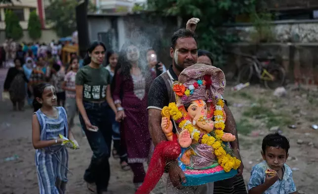 A devotee carries an idol of the elephant-headed Hindu god Ganesha with others for immersion in a makeshift pond during Ganesh Visarjan in New Delhi, India, Friday, Sept. 25, 2026. (AP Photo/Manish Swarup)