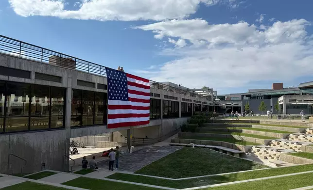 FILE - People gaze down at the site where Charlie Kirk was shot, above which hangs an American flag, at Utah Valley University, Sept. 15, 2025, in Orem, Utah. (AP Photo/Jesse Bedayn, File)