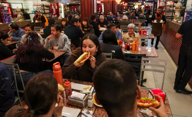 Antonia Bravo eats a "completos", traditional Chilean hot dogs topped with mashed avocado, diced tomatoes and mayonnaise, at the "El Portal Ex Bahamondes" restaurant in downtown Santiago, Chile, Thursday, Sept. 10, 2026. (AP Photo/Esteban Felix)