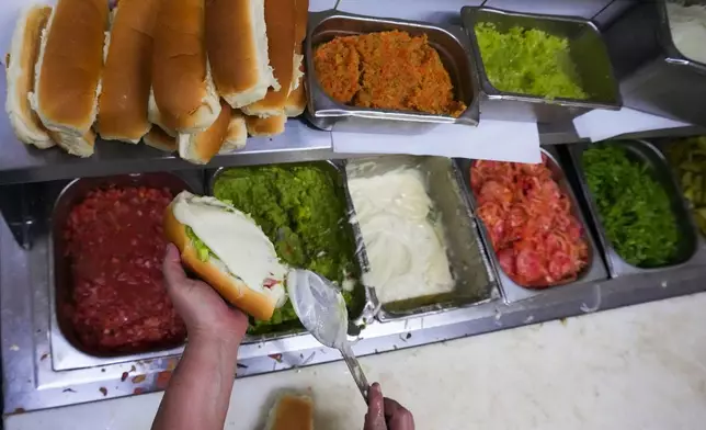 A cook prepares "completos", traditional Chilean hot dogs topped with mashed avocado, diced tomatoes and mayonnaise, at a restaurant in Santiago, Chile, Monday, Sept. 14, 2026. (AP Photo/Esteban Félix)