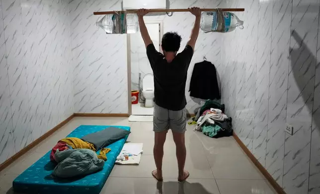 A rescued Vietnamese scam worker shows how he exercises using improvised weights made of a wooden stick and water jugs as he waits to be repatriated at the Presidential Anti-Organized Crime Commission temporary detention center, a former scam compound in Pasay, Philippines, Tuesday, June 3, 2025. (AP Photo/Aaron Favila)