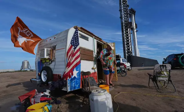 David Orr camps out near the site where SpaceX's mega rocket Starship, behind right, is preparing for a test flight from Starbase, Texas, Sunday, Sept. 27, 2026. (AP Photo/Eric Gay)