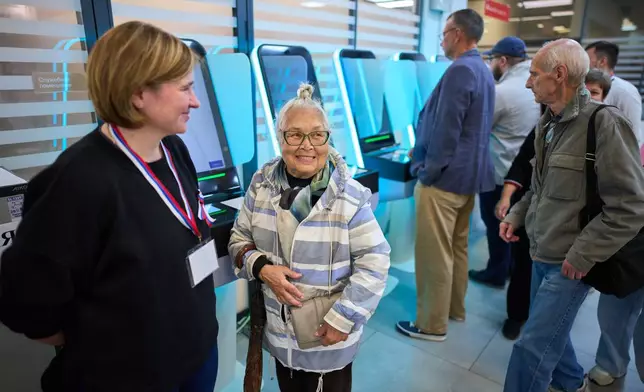 A woman smiles as she speaks to an election commission employee, left, after using an electronic voting system in the parliamentary election in Moscow, Russia, Saturday, Sept. 19, 2026. (AP Photo/Alexander Zemlianichenko)