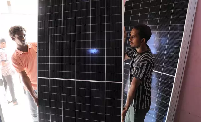 Workers carry a panel ready for installation at a solar energy systems store in Omdurman, on the outskirts of Khartoum, Sudan, July 23, 2026. (AP Photo/Mohnd Blal)