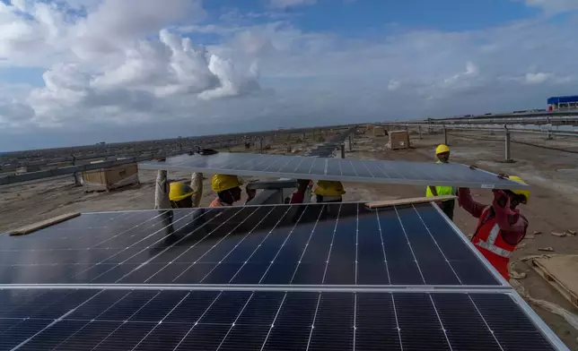 FILE - Workers install solar panels at the under-construction Adani Green Energy Limited's Renewable Energy Park in the salt desert of Karim Shahi village, near Khavda, Bhuj district near the India-Pakistan border in the western state of Gujarat, India, Sept. 21, 2023. (AP Photo/Rafiq Maqbool, File)