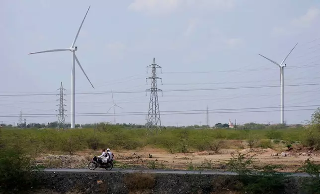 FILE - A motorcyclist ride past wind turbines, an Adani Group project, near Sadla village in Surendranagar district of Gujarat state, India, March 20, 2023. (AP Photo/Ajit Solanki, File)