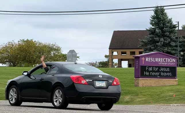 A driver waves while passing in front of Resurrection Lutheran Church and its church sign, featuring a seasonal pun, in Woodbury, Minn., on Sunday, Sept. 27, 2026. (AP Photo/Giovanna Dell'Orto)