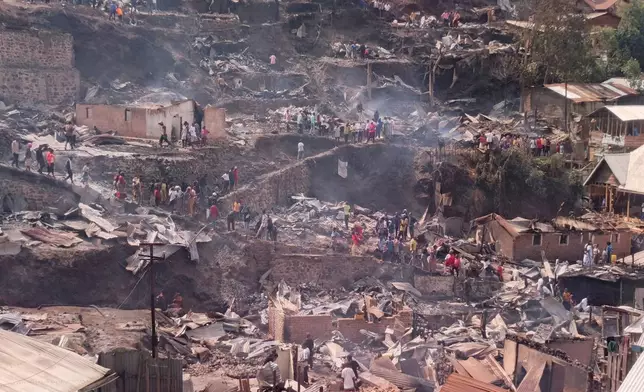 People walk amid the charred remains of homes near a primary school and a secondary school where a fire broke out, killing several students, in Bukavu, Congo, Thursday, Sept. 10, 2026. (AP Photo/Janvier Barhahiga)