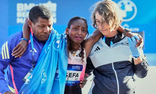 Ethiopia's Tigist Assefa is lead away by former runner Haile Gebrselassie, left, and a medical after winning the Berlin Marathon in Berlin, Germany, Sunday, Sept. 27, 2026. (AP Photo/Ebrahim Noroozi)