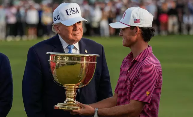 President Donald Trump smiles as USA teams' Jackson Koivun holds the Presidents Cup trophy after the Presidents Cup golf tournament against the International team at Medinah Country Club, Sunday, Sept. 27, 2026, in Medinah, Ill. (AP Photo/Chris Carlson)