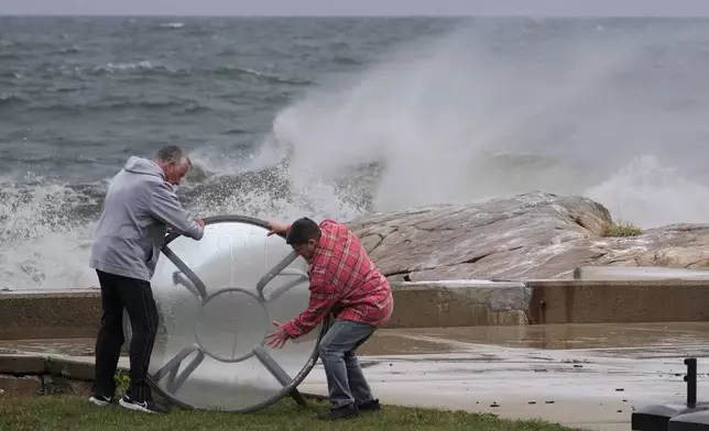 John Garrisi, left, and Gaige Graf move an outdoor table away from the shorefront during the early stages of a nor'easter storm, Friday, Sept. 25, 2026, in Gloucester, Mass. (AP Photo/Robert F. Bukaty)