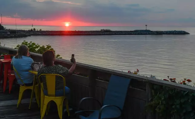 People watch the sun set over Lake Ontario, Tuesday, Aug. 25, 2026, in Olcott, N.Y. (AP Photo/Adrian Kraus)