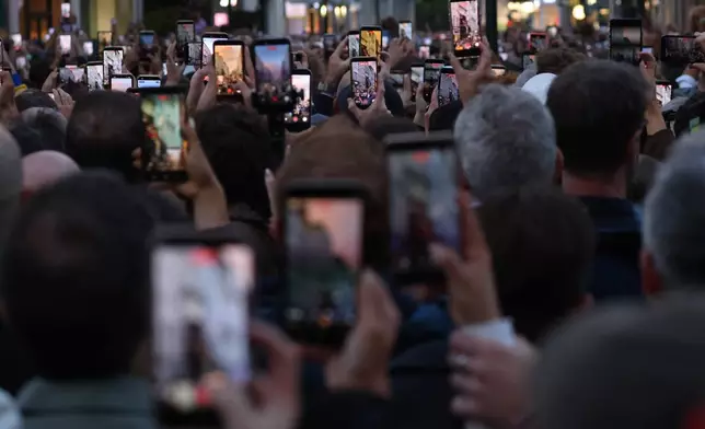 Members of the crowd take photos on their phones as U2 perform an impromptu concert from a balcony in central Dublin, Ireland , Friday, Sept. 25, 2026. (AP Photo/Peter Morrison)
