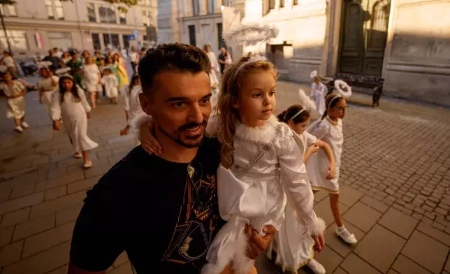A man holds a child dressed as an angel during an event dubbed the Little Angels' Parade, a Christian-themed street performance featuring dozens of children wearing angel costumes, in Bucharest, Romania, Saturday, Sept. 5, 2026. Sept. 5, 2026. (AP Photo/ Andreea Alexandru)