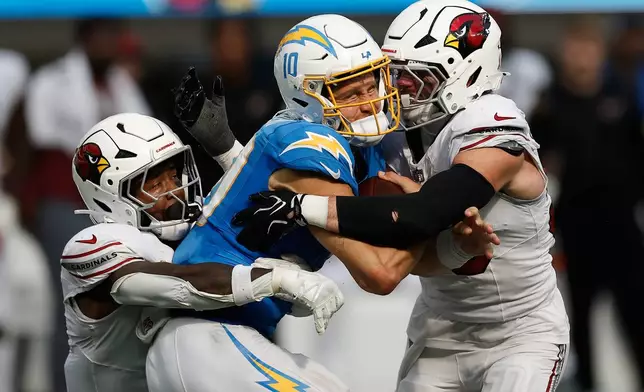 Los Angeles Chargers quarterback Justin Herbert, middle, is sacked by Arizona Cardinals safety Budda Baker, left, and linebacker Jack Gibbens during the second half of an NFL football game, Sunday, Sept. 13, 2026, in Inglewood, Calif. (AP Photo/Caroline Brehman)