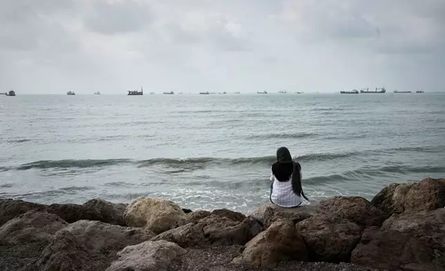 A woman relaxes along the rocky shoreline as commercial vessels lie anchored off Bandar Abbas, Iran, Friday, Sept. 4, 2026. (AP Photo/Vahid Salemi)