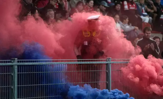 A policeman is engulfed in colored smoke from smoke bombs thrown onto the pitch during the women's Champions League opening phase soccer match between FC Bayern Munich and Manchester City in Munich, Germany, Tuesday, Sept. 22, 2026. (AP Photo/Matthias Schrader)