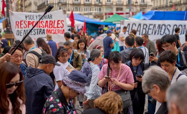 Tourists gather in front of protesters camping during a protest at Sol Square following the eviction last Wednesday of 87-year-old Maricarmen as they demand stronger laws to protect renters in Madrid, Spain, Monday, Sept. 28, 2026. (AP Photo/Manu Fernandez)