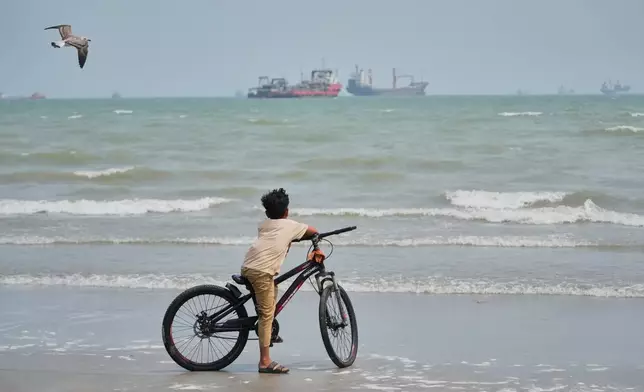 A gull flies overhead as a boy stands with his bicycle on a beach overlooking commercial vessels anchored in the Strait of Hormuz off Bandar Abbas, Iran, Monday, Sept. 7, 2026. (AP Photo/Vahid Salemi)
