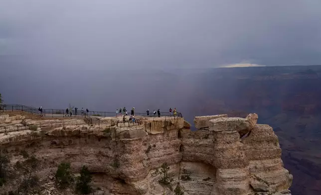 People stand at the rim of the Grand Canyon as rain moves into the canyon, Monday, Aug. 31, 2026, in Grand Canyon National Park, Ariz. (AP Photo/John Locher)