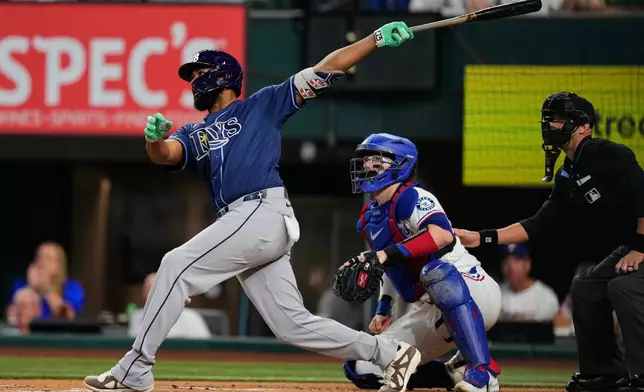 Tampa Bay Rays' Junior Caminero follows through on a solo home run swing as Texas Rangers catcher Danny Jansen and umpire Will Little look on in the first inning of a baseball game Saturday, Sept. 5, 2026, in Arlington, Texas. (AP Photo/Tony Gutierrez)
