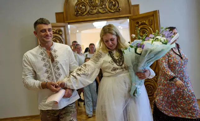 Newly-married couple Liudmyla Ryzhak, right, and her husband Leonid Ryzhak leave after getting married, following a Russian missile and drone attack in Kyiv, Ukraine, Tuesday, Sept. 8, 2026. (AP Photo/Francisco Seco)