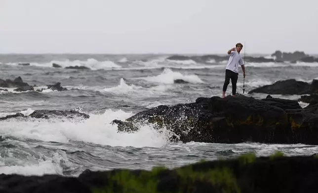 Chase Gabin fishes among the rocks as Hurricane Nolo sits nearby Friday, Sept. 25, 2026, in Hilo, Hawaii. (AP Photo/Gregory Bull)