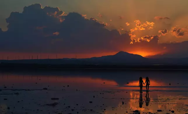 Girls are silhouetted against a salt lake as the sun sets in the southern coastal city of Larnaca, on the eastern Mediterranean island of Cyprus, Wednesday, Sept. 23, 2026. (AP Photo/Petros Karadjias)