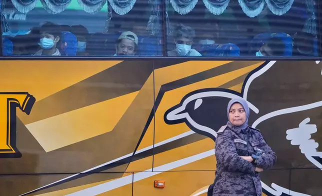 Myanmar nationals look out from a bus in Manjung, Perak state of Malaysia, on Tuesday, Sept. 29, 2026, as a uniformed official walks past. (AP Photo/Vincent Thian)