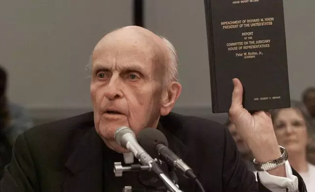 FILE - Former Massachusetts Rep. Father Robert Drinan holds a copy of the 1974 impeachment report of President Nixon while testifying before the House Judiciary Committee's impeachment hearing on Capitol Hill in Washington, on Dec. 8, 1998. (AP Photo/J. Scott Applewhite, File)