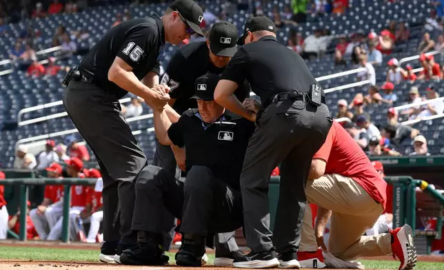 Home plate umpire Todd Tichenor, center, is helped up after being hit by a foul tip by Los Angeles Angels' Wade Meckler during the first inning of a baseball game between the Washington Nationals and the Angels, Sunday, Sept. 13, 2026, in Washington. (AP Photo/Nick Wass)
