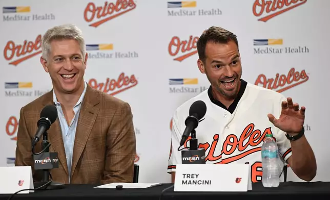 Former Baltimore Oriole Trey Mancini, right, waves to his daughter before signing a one day contract with Baltimore Orioles general manager Mike Elias and returning to the team as he announces his retirement during a news conference on Saturday, Sept. 19, 2026 in Baltimore. (AP Photo/Gail Burton)