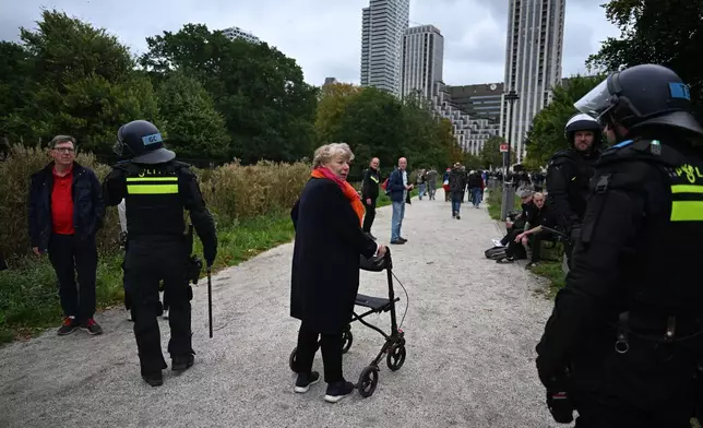 A woman walks past police officers during a far-right groups' protest against immigration and asylum policies, in The Hague, Netherlands, Saturday, Sept. 19, 2026. (AP Photo/Mouneb Taim)