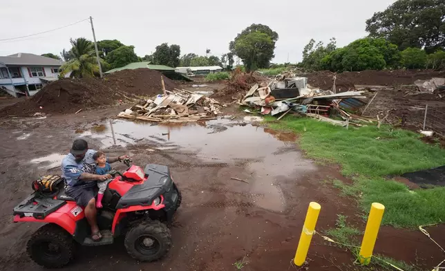 A man rides with his son near where a home was destroyed during last month's Hurricane Lala, as floodwaters from Hurricane Nolo recedes Sunday, Sept. 27, 2026, in Naalehu, Hawaii. (AP Photo/Gregory Bull)