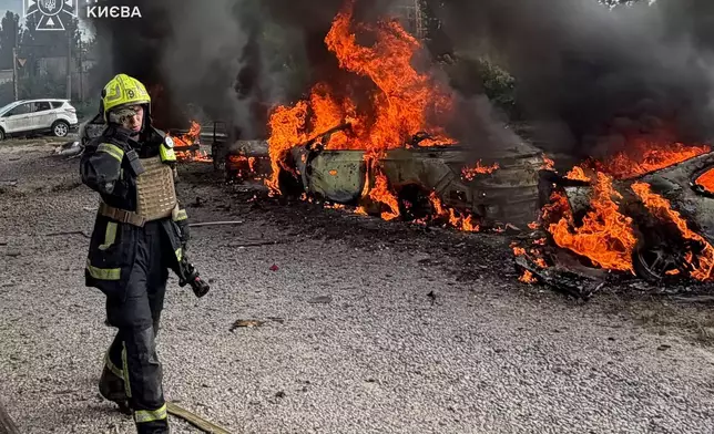 In this photo provided by the Ukrainian Emergency Service, a firefighters walk past burning cars as they work at the site, following a Russian air attack in Kyiv, Ukraine, Wednesday, Sept. 16, 2026. (Ukrainian Emergency Service via AP)