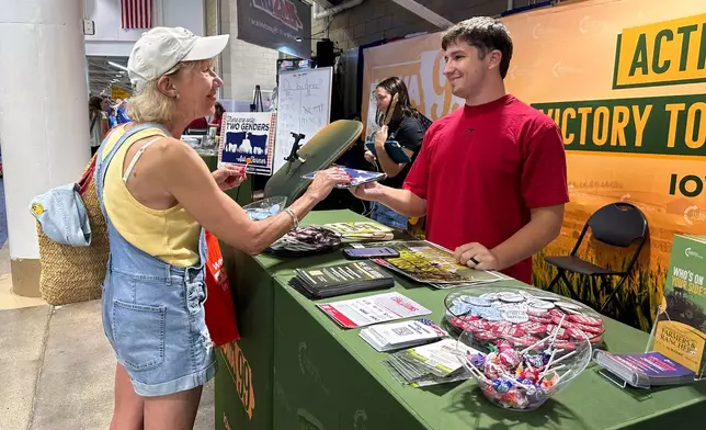 A Turning Point Action staffer gives an American flag to a voter at the Iowa State Fair in Des Moines, Iowa, Friday, Aug. 21, 2026. (AP Photo / Hannah Fingerhut)