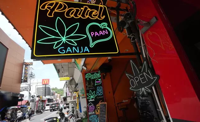 Workers clean a road next to a sign of a cannabis shop in Pattaya, Thailand, Tuesday, Sept. 1, 2026. (AP Photo/Sakchai Lalit)