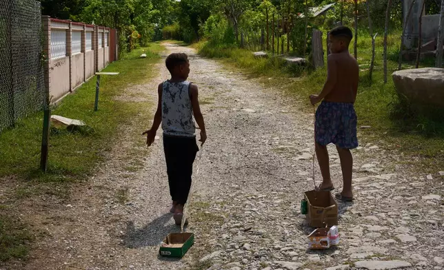 Children drag toys made from cardboard boxes as they walk in Minas, in Cuba's Havana province, Monday, Aug. 31, 2026. (AP Photo/Ramon Espinosa)