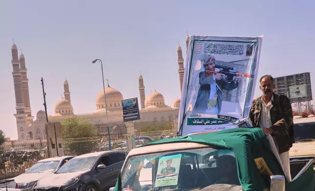 A man stands beside a portrait of Houthi fighter Mohammed Omar Ali al-Saqqaf, also known as Abu Fatima, mounted on a pickup truck during a mass funeral procession, with Al-Saleh Mosque in the background, in Sanaa, Yemen, Wednesday, Sept. 16, 2026. (AP Photo)