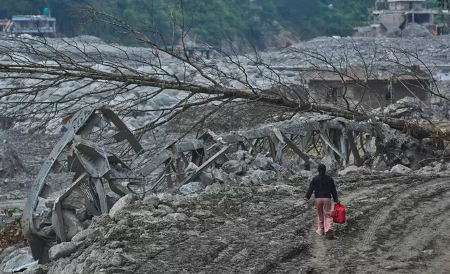 A woman walks past a damaged bridge and trees left by a flash flood on the bank of the Trishuli River in Nuwakot district, Nepal, Wednesday, Sept. 23, 2026. (AP Photo/Niranjan Shrestha)
