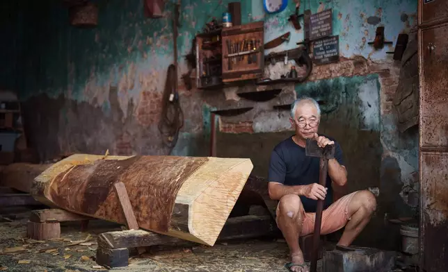 Goh Khuay Hou sits with an axe during the early stages of making a Mei Hua coffin at his family's workshop in Muar, Malaysia, Monday, Sept. 7, 2026. (AP Photo/Vincent Thian)