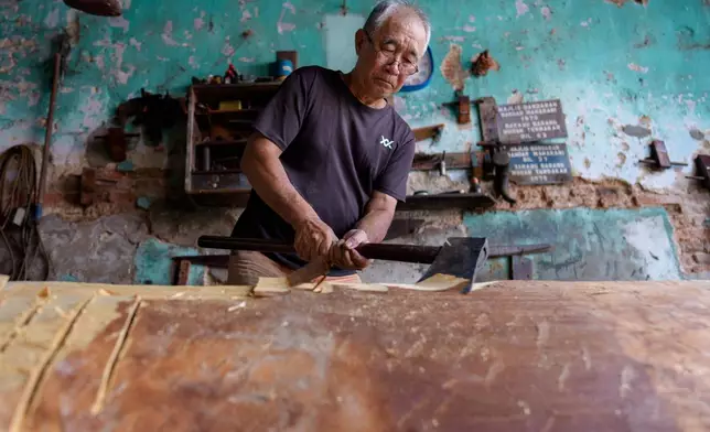 Goh Khuay Hou uses an axe to shape a wooden section during the early stages of making a Mei Hua coffin at his family's workshop in Muar, Malaysia, Monday, Sept. 7, 2026. (AP Photo/Vincent Thian)