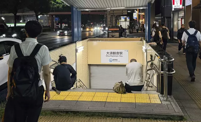 People sit in front of a shuttered entrance to a subway station after all train services were suspended due to a heavy rain in Nagoya, central Japan Tuesday, Sept. 8, 2026. (Shigeyuki Inakuma/Kyodo News via AP)
