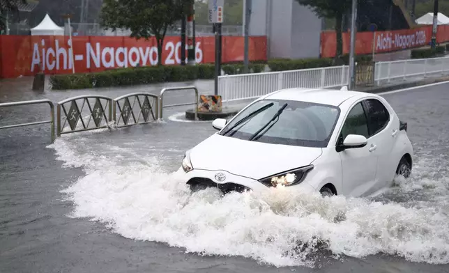 A car drives along a flooded road following heavy rain with a banner for the Aichi-Nagoya Asian Games in the background in Nagoya, central Japan, on Tuesday, Sept. 8, 2026. (Natsumi Yasumoto/Kyodo News via AP)