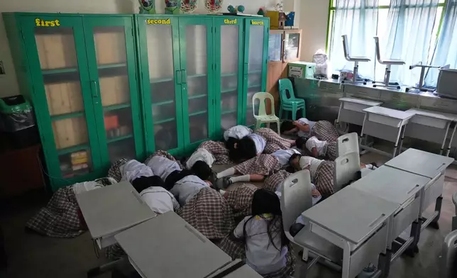 Students lay on the floor inside their classroom as they take cover during a nationwide school safety drill in San Rafael, Bulacan province, Philippines, Thursday, Sept. 3, 2026. (AP Photo/Aaron Favila)